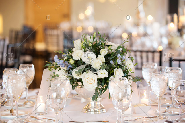 White floral centerpiece and wine glasses on dining table at wedding reception