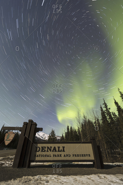 The Aurora Borealis (Northern Lights) and stars circling above the sign marking the entrance to Denali National Park and Preserve, Alaska, United States of America
