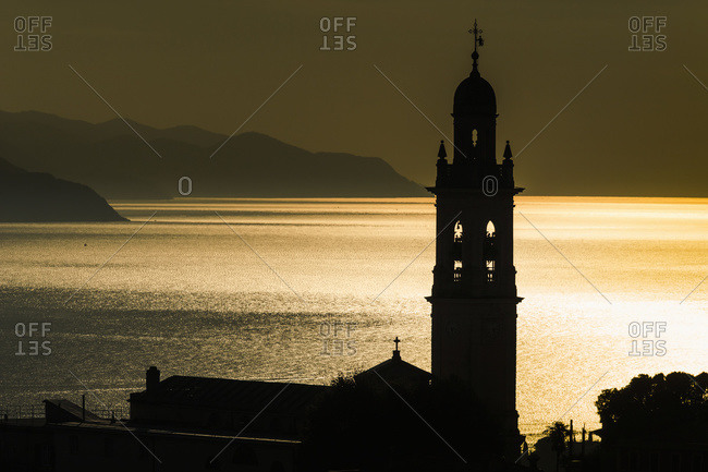 Golden sunlight reflected on water at dusk with tower of church, San Lorenzo della Costa, Liguria, Italy