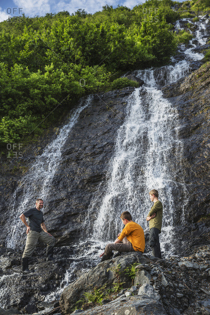 Man with two teenage boys on the rocks in front of a waterfall at Shoup Bay State Marine Park, Prince William Sound, Valdez, Alaska, United States of America