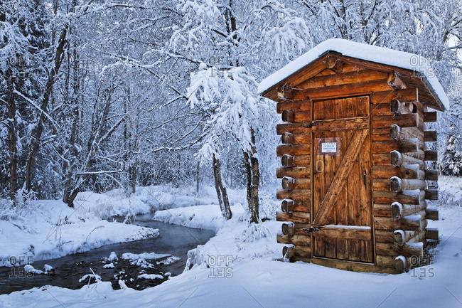 Log outhouse by a meandering creek in snow, Chena Hot Springs Resort, Fairbanks, Alaska, United States of America