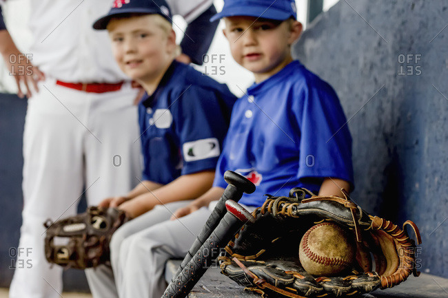 A closeup focus on a game used baseball and glove with young boy players in uniform sitting on the dugout bench in the background, Fort McMurray, Alberta, Canada