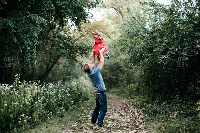 Father lifting young daughter in red dress on forest path in fall