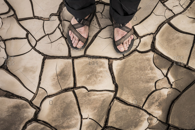 Feet in sandals standing on cracked mud
