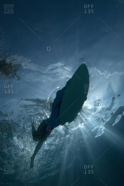 An underwater silhouette of a child riding a boogie board with blue water and blue skies