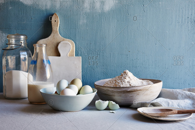 Still life with cutting board, jars of ingredients, fresh eggs and bowl of flour
