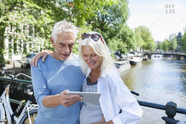 Senior couple with digital tablet at town canal