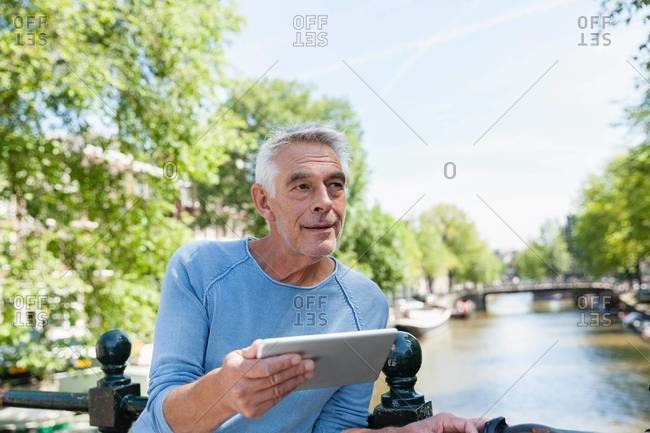 Senior man with digital tablet at town canal