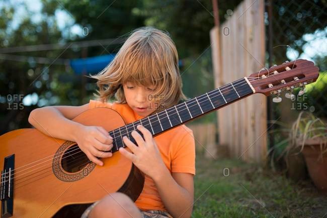 Long-haired blond boy playing spanish guitar outdoors