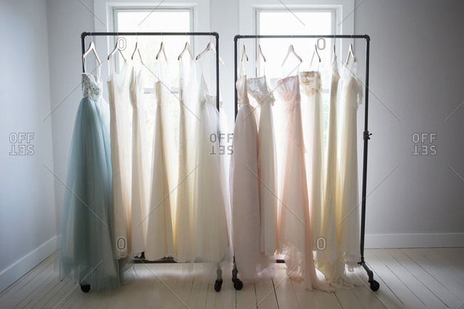 Two racks of wedding gowns on racks in front of window
