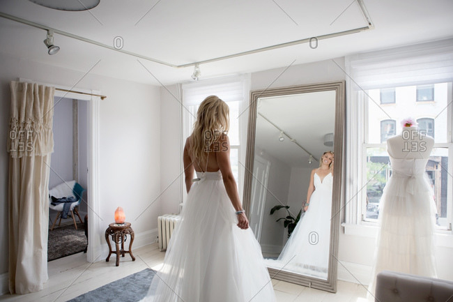Woman trying on wedding dress admires her reflection in mirror