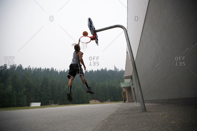 Man dunking a basketball in rural parking lot