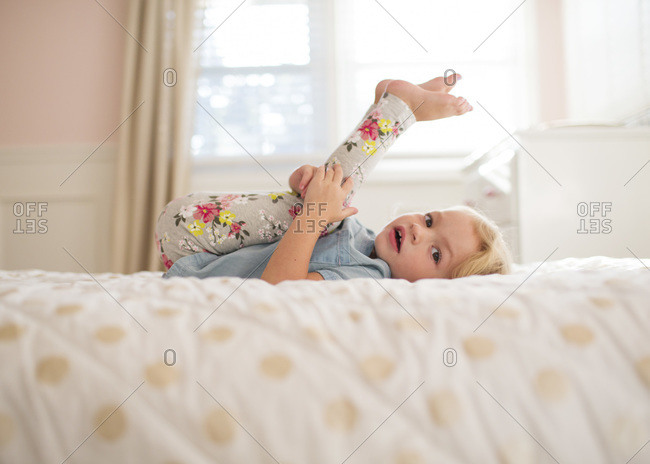 A girl pulls her legs over her head on her bed