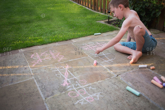 Boy drawing tic tac toe boards on sidewalk with chalk
