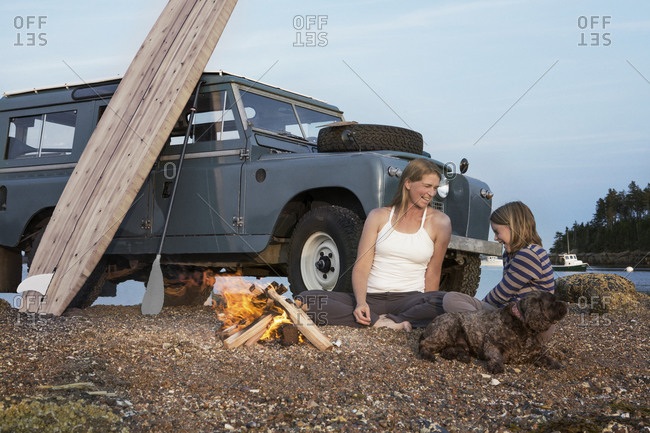 Laughing mother and daughter with dog by beach campfire