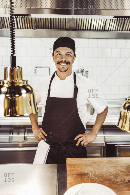 Portrait of happy male chef standing with hands on hips in a commercial kitchen