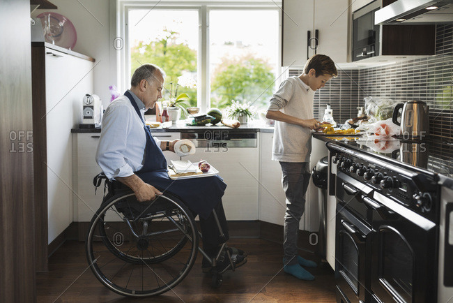 Son with disabled father cutting vegetables in a kitchen