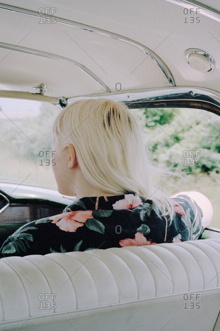 Back view of woman with dyed platinum blond hair in flowered shirt in front seat of classic car