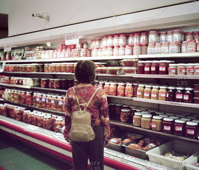 Woman looking at jars of food in refrigerated case of market