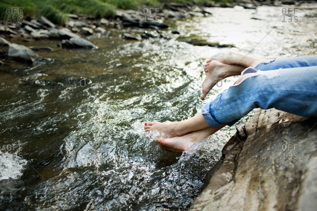 A woman in fashionable jeans with a rip, with her feet in the cool flowing waters of a river