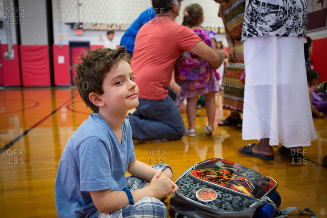 Young boy sitting on school gymnasium floor with his backpack
