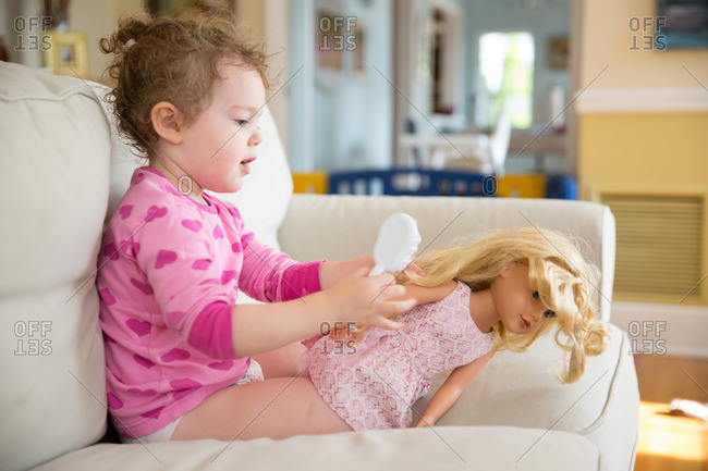Toddler girl combing hair of her doll