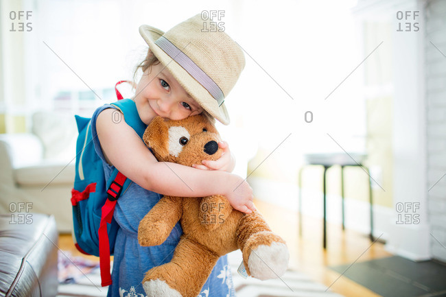 Girl in hat with backpack hugs her stuffed animal