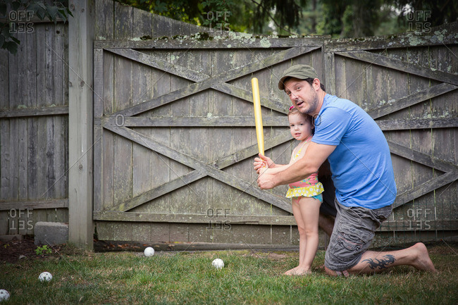 Father stands at bat with his daughter in a game of wiffle ball
