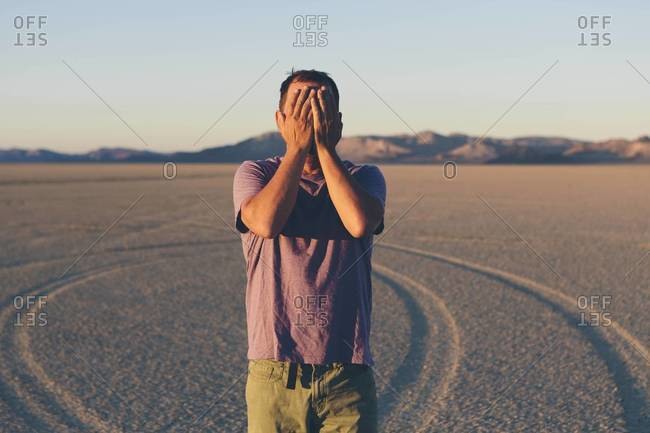 Man standing in the desert and covering his face in Black Rock Desert, Nevada at dawn