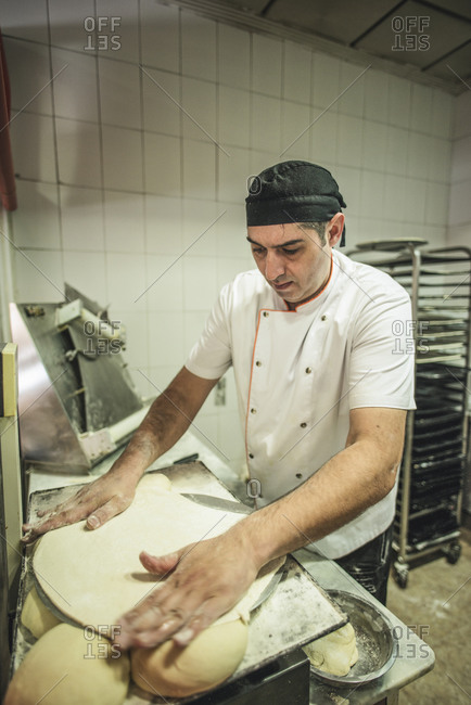 Experienced pizza baker preparing dough for pizza in his bake shop