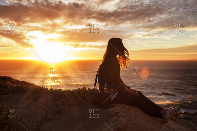 Woman sitting and watching sunset over the ocean