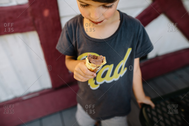 A boy looks down at half eaten chocolate ice cream cone