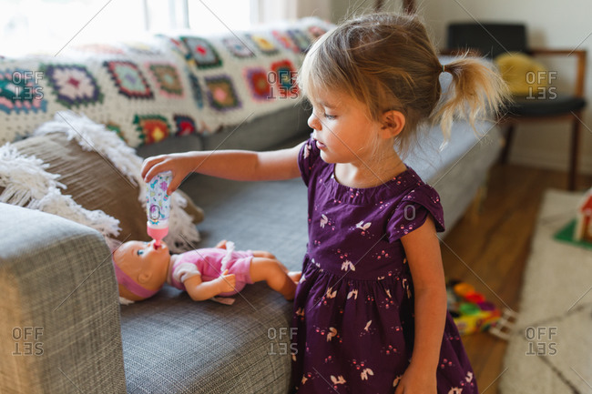 Young girl giving her baby doll a bottle on sofa