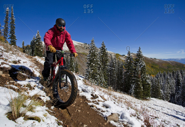 A man wearing red rides a fat tire bike along a trail surrounded by snow during the fall in Utah
