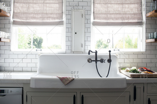 Rustic white porcelain apron kitchen sink with rubbed oil bronze faucet and subway tile backsplash under windows