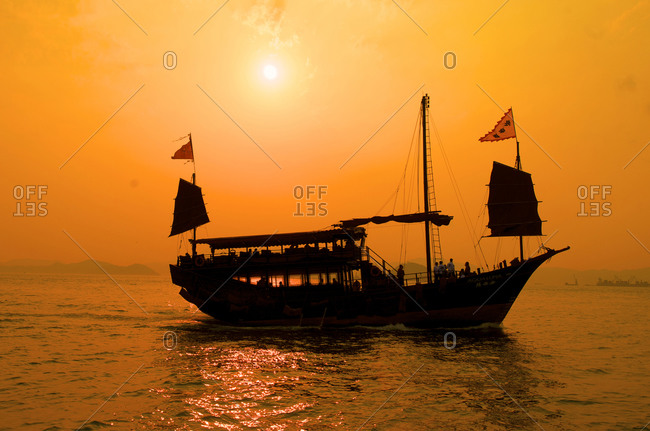 A junk sails through Aberdeen harbor near Hong Kong at sunset, Hong Kong, China