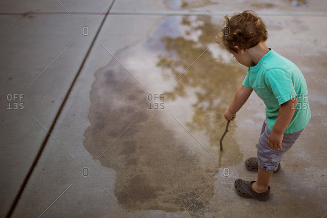 Boy poking a stick into puddle on concrete