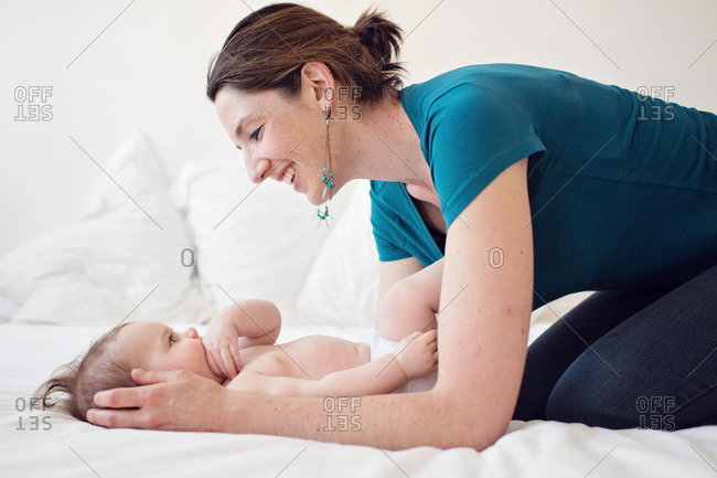 Mother crouching over her baby on a white bed