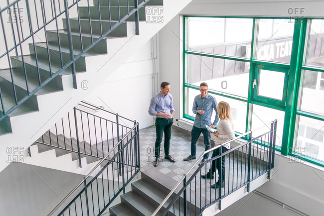 Three colleagues talk in bright stairwell of office building