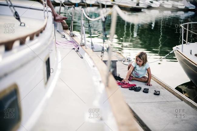 Young girl sitting on marina doc plays with flip flops