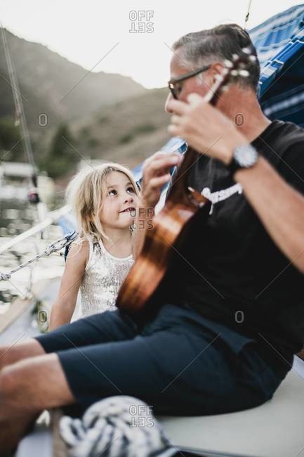 Girl listening to father playing ukulele on sailboat