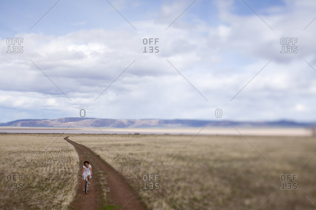 Woman riding a bike on a desolate dirt road under a cloudy sky