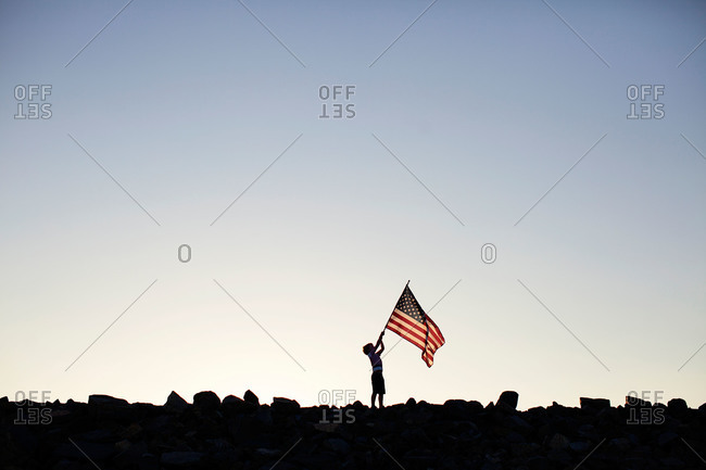 Silhouette of boy with American flag on rocks