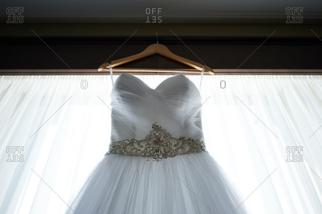 Close-up of a wedding dress hanging in front of a window