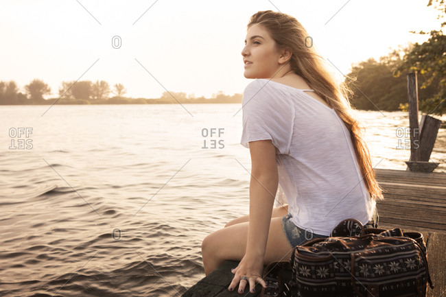 Woman sitting on dock with feet in water at dusk