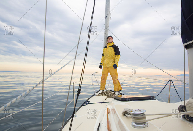 Senior man in yellow rain gear stands on deck of sailboat