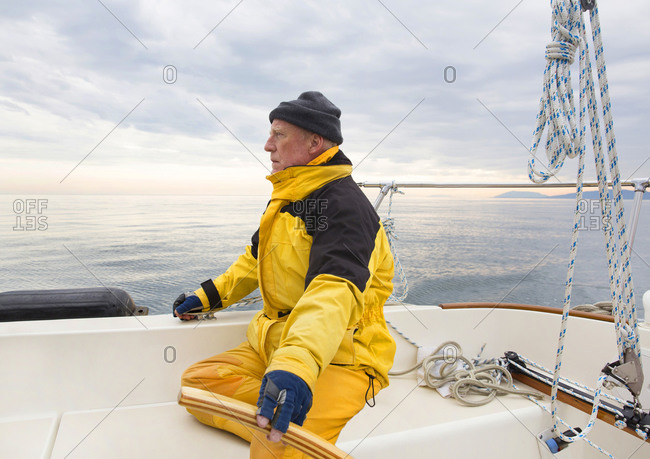 Senior man in yellow train gear with his hand on the till of his sailboat