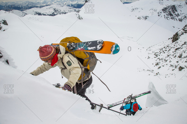 Skiers boot pack with gear on their back up a steep slope to a notch in the Coast Mountains during the Spearhead Traverse in Whistler, British Columbia, Canada