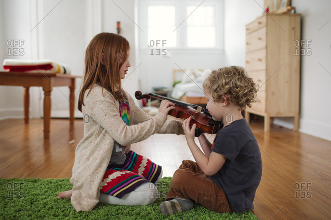 Young girl showing her brother how to hold a violin