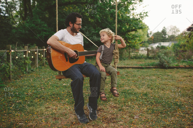 Father and son playing guitar on a swing